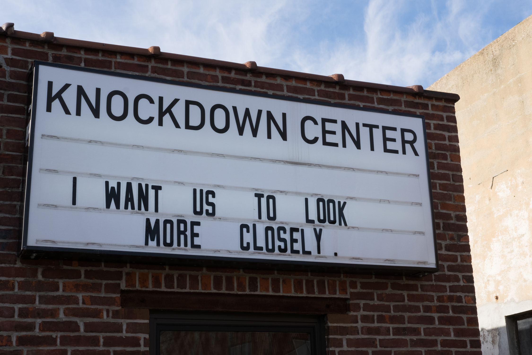 The marquee sign in front of the Knockdown Center reads "I want us to look more closely"