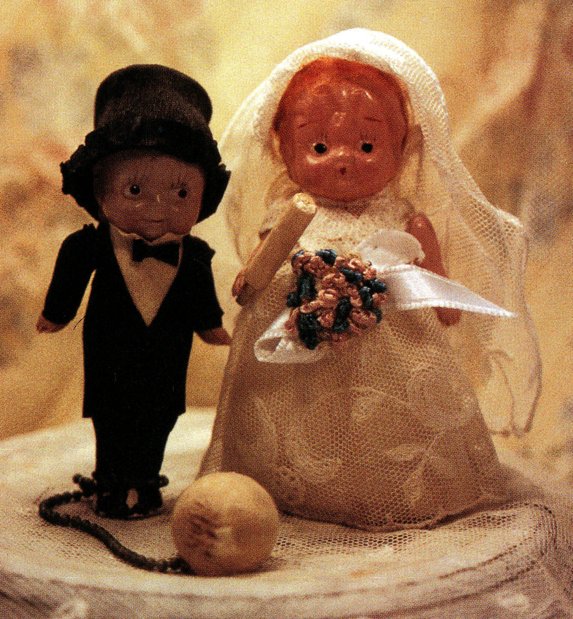 Childlike dolls. The groom doll wears a chain around his ankle leading to a big white cement-like ball.
