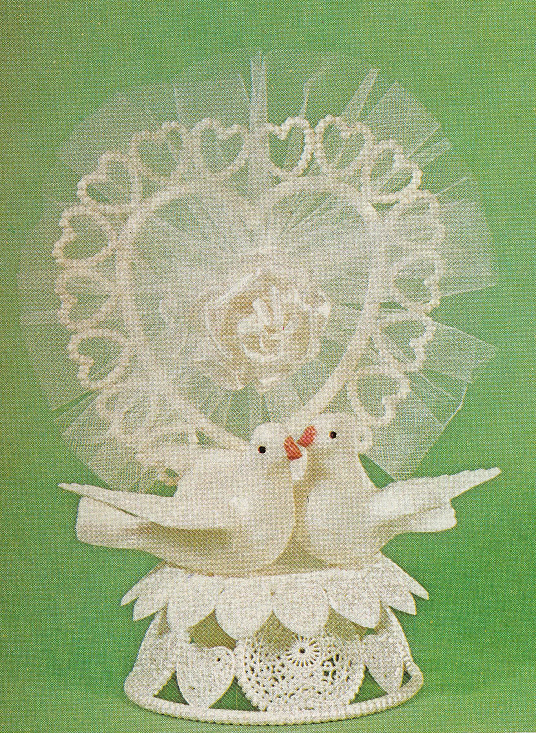 Two white doves in front of a heart-shaped plastic pearl arch, under a dangling tulle bow