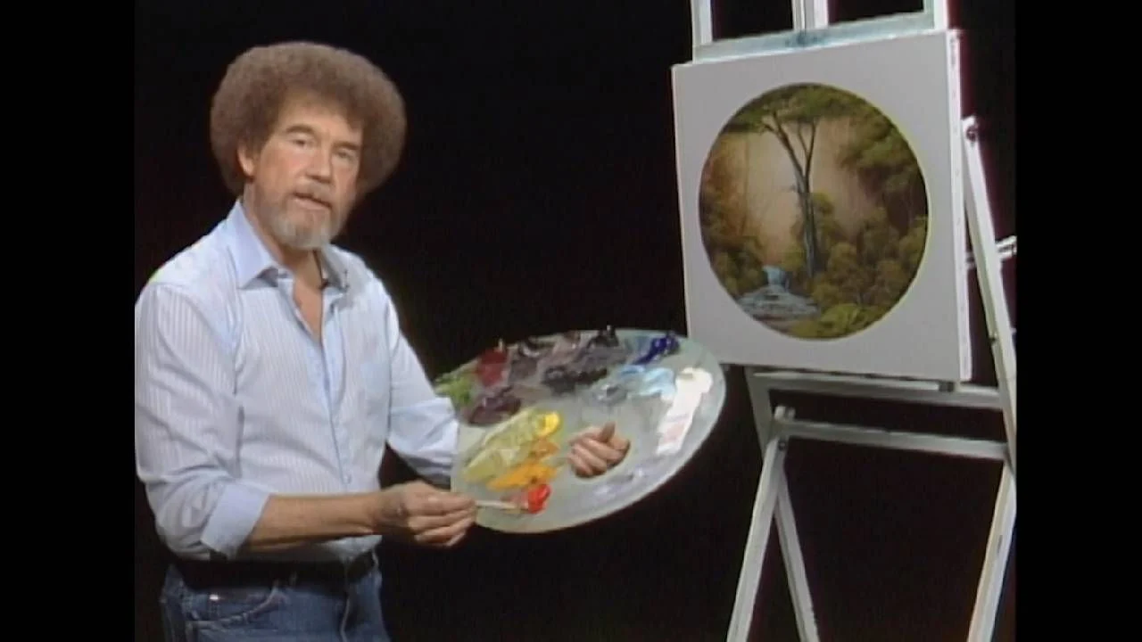 Bob Ross stands in front of a painting of a tree in progress, holding a palette and looking toward the camera.