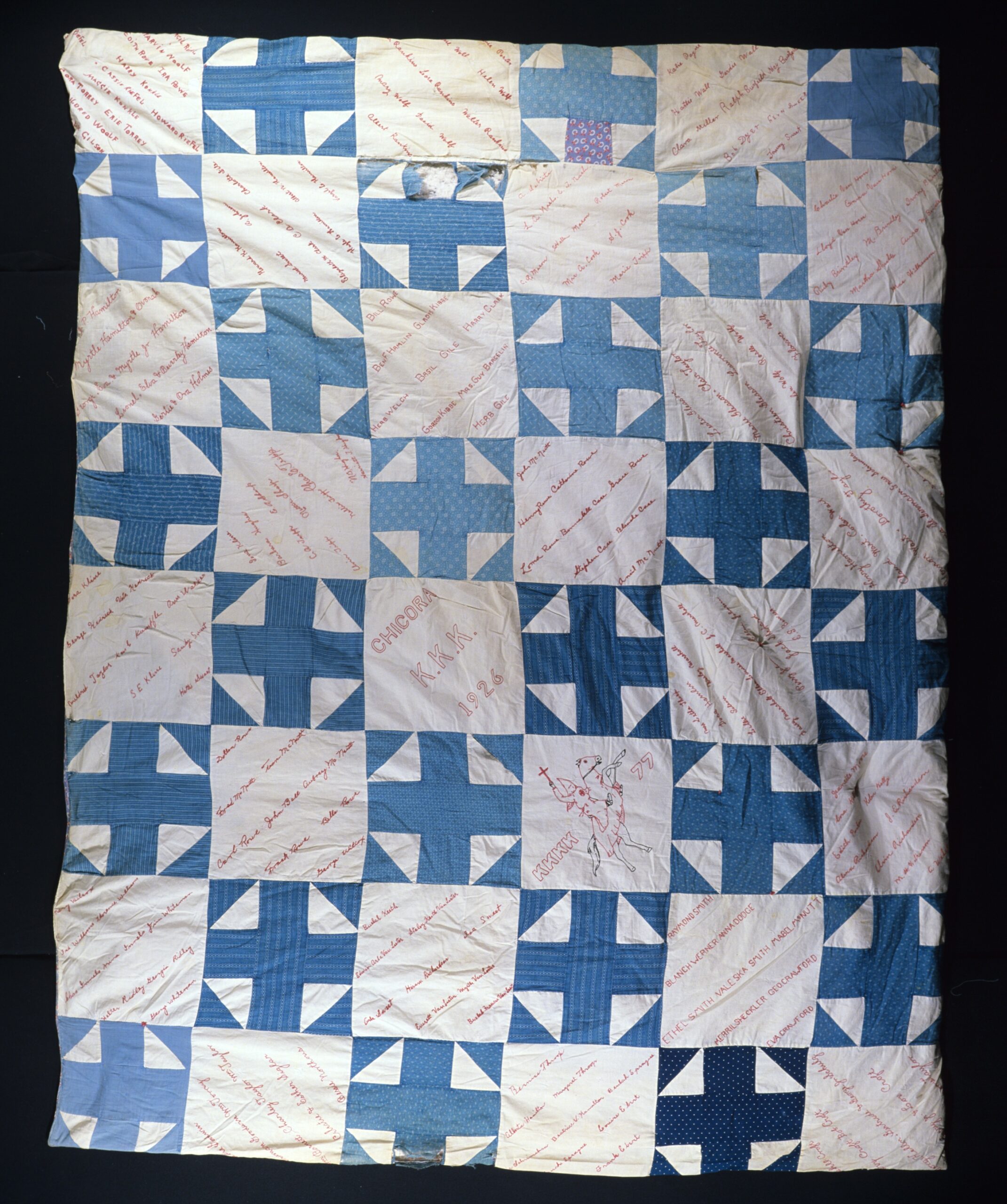 quilt with alternating squares of blue crosses and white squares embroidered with names in black and red