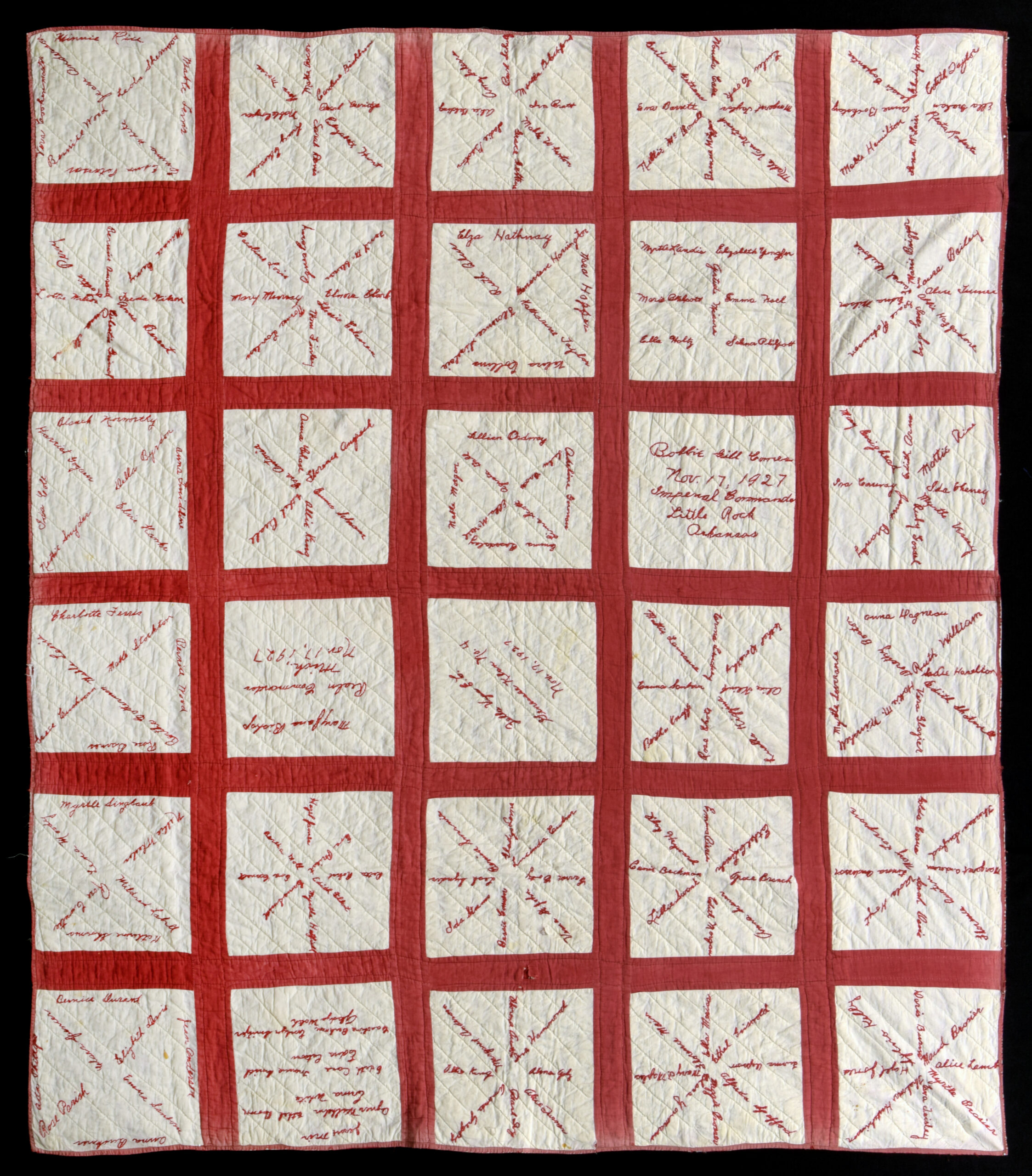 quilt composed of white squares with red embroidered names overlaid, enclosed by red borders
