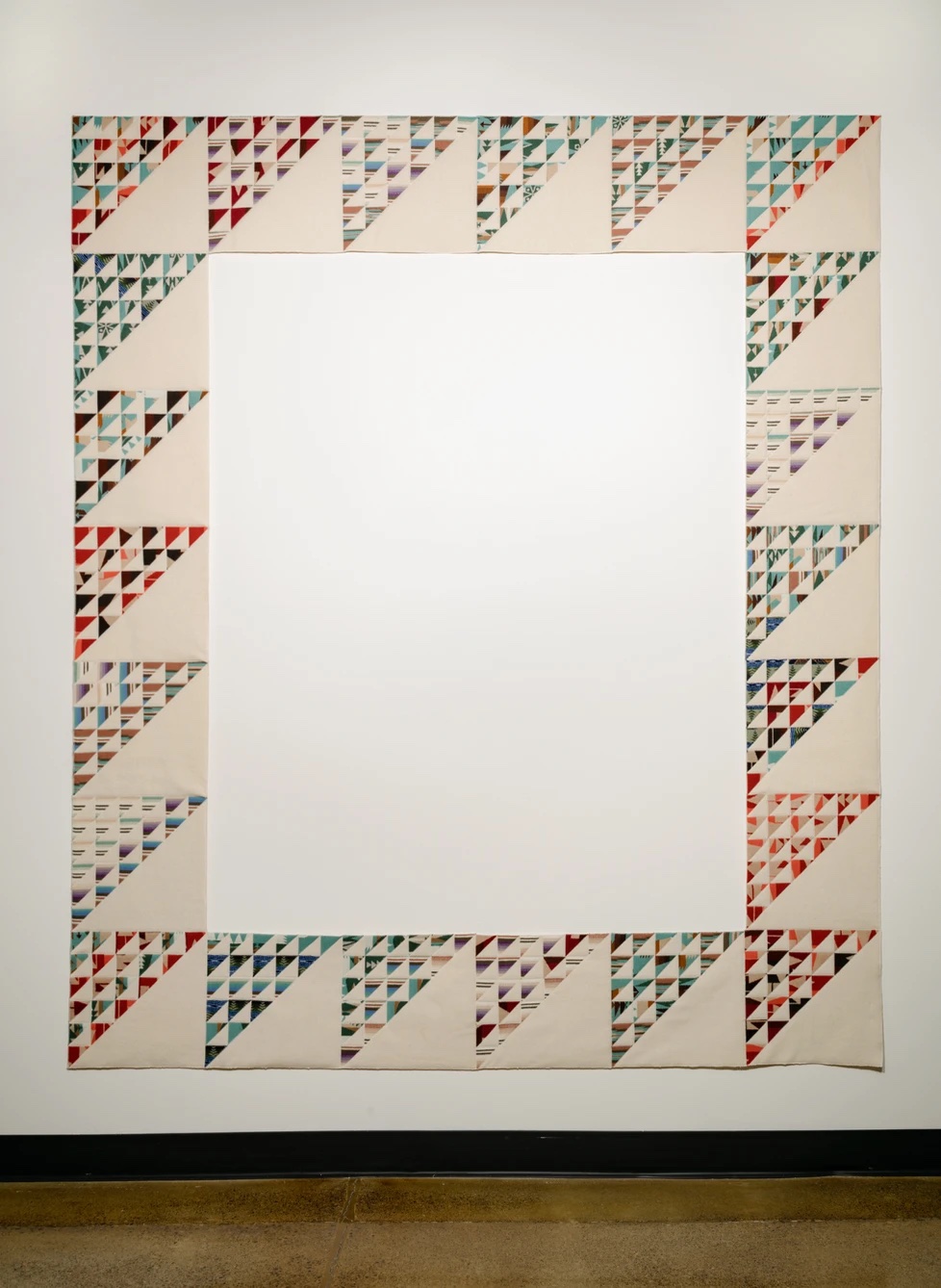 the pieced border of a quilt with an empty interior, against a white wall