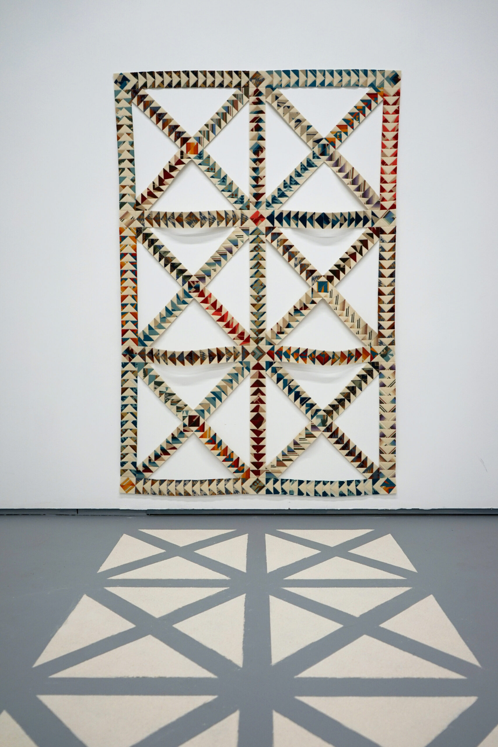fabric lattice resembling empty quilt blocks on the wall, with flour on the floor in front of it laid out in the pattern of the missing sections