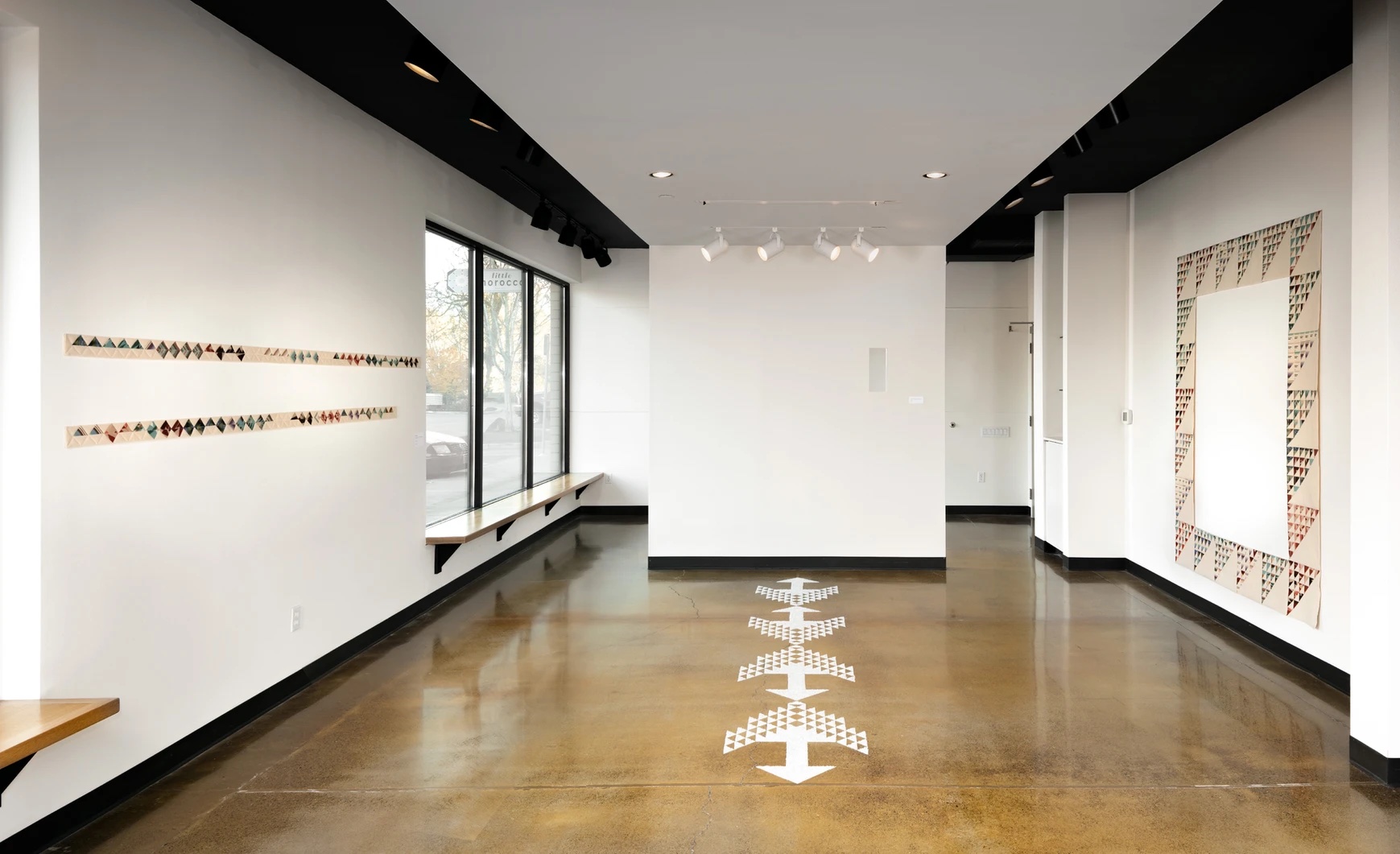 a long white gallery with quilts on the walls and white markings on the wood floor