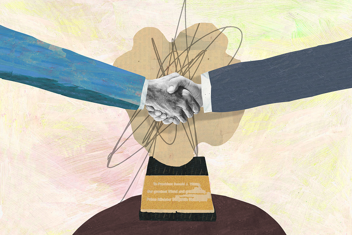 two arms shake hands in front of a wooden trophy on a small table