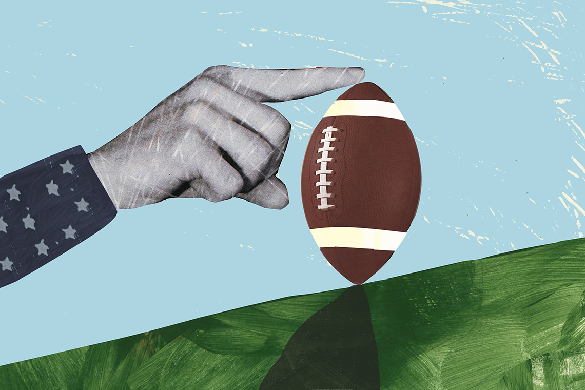 a hand with outstretched finger balances a football on a green slope